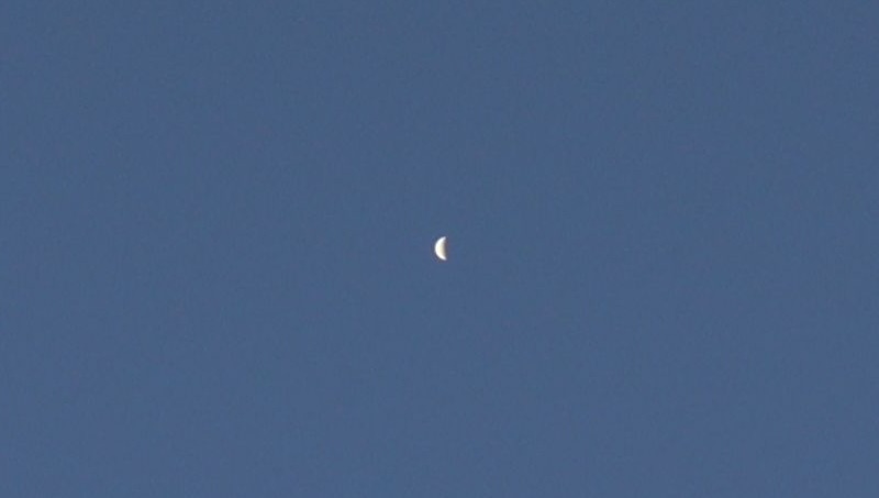 An almost half-illuminated disk of the planet Venus against a deep blue sky.