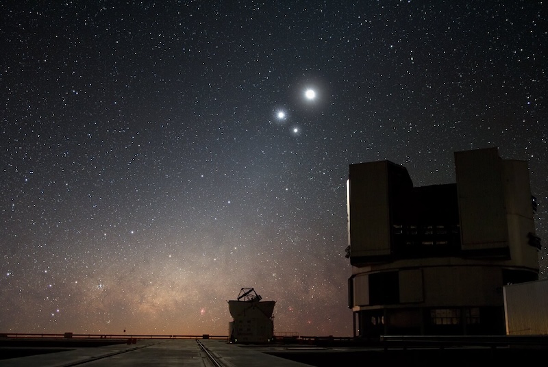 2 telescopes in silhouette, with 3 bright spots in the night sky above them.