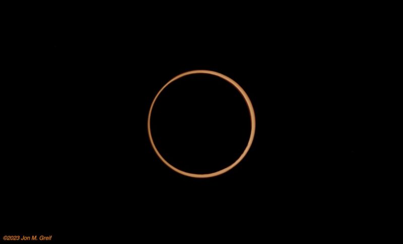 A thin ring of orange amidst black; the ring is slightly thinner on the left.