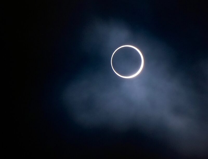 Black circle with a white ring around it. There are some clouds at the bottom right of the image.
