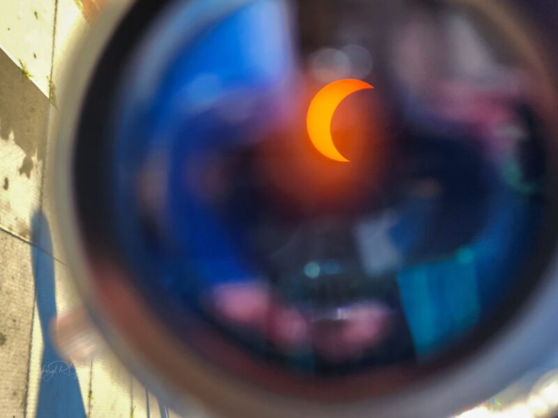 Closeup of the surface of a lens with a sharp-edged orange crescent amid murky reflections.