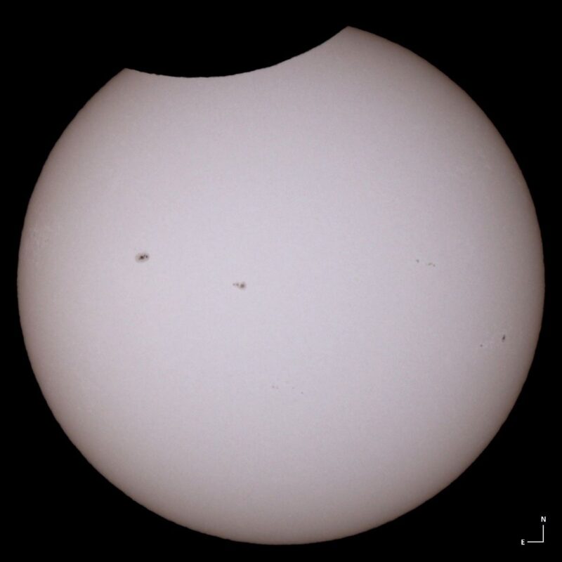 On black background, a round sun with minor bite taken out of it and 2 or 3 small dark spots on it.