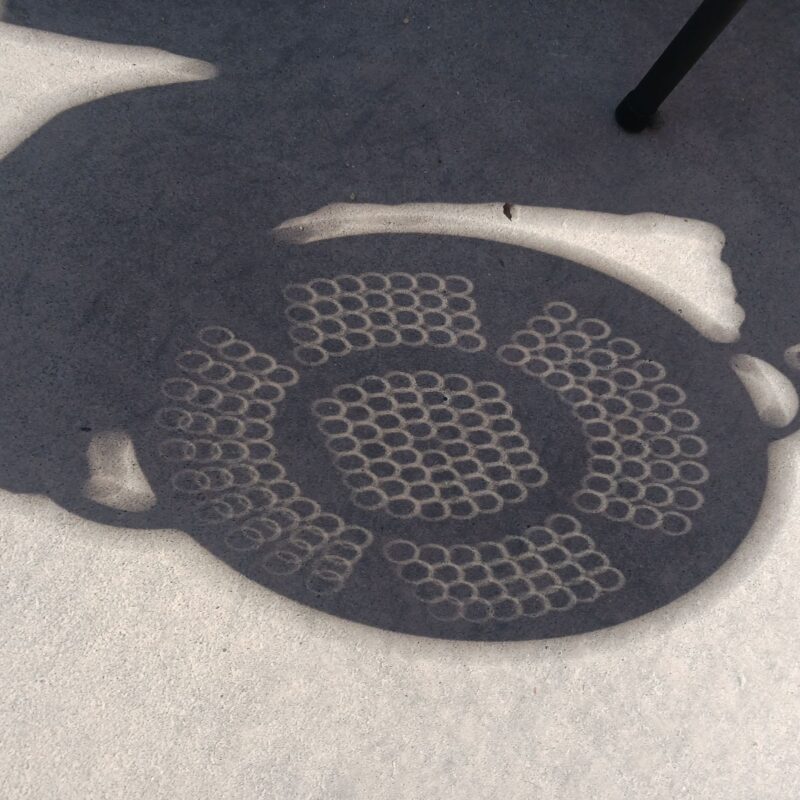 The shadow of a colander on the floor. There are tens of tiny circles inside the colander shadow.