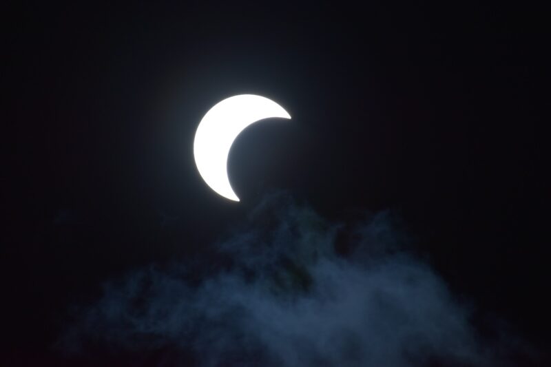 A bright white crescent on a dark background with faint clouds.