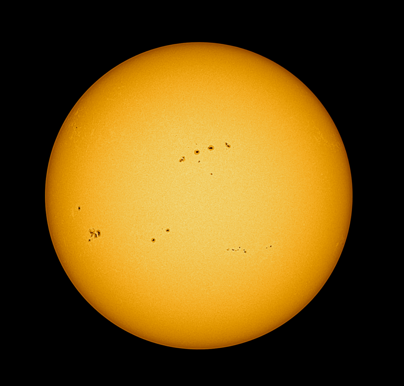 The sun, seen as a large yellow sphere with a smooth surface and dark spots.
