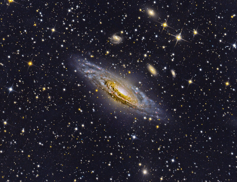 Large, oblique spiral galaxy and some smaller spiral and elliptical galaxies nearby in star field.