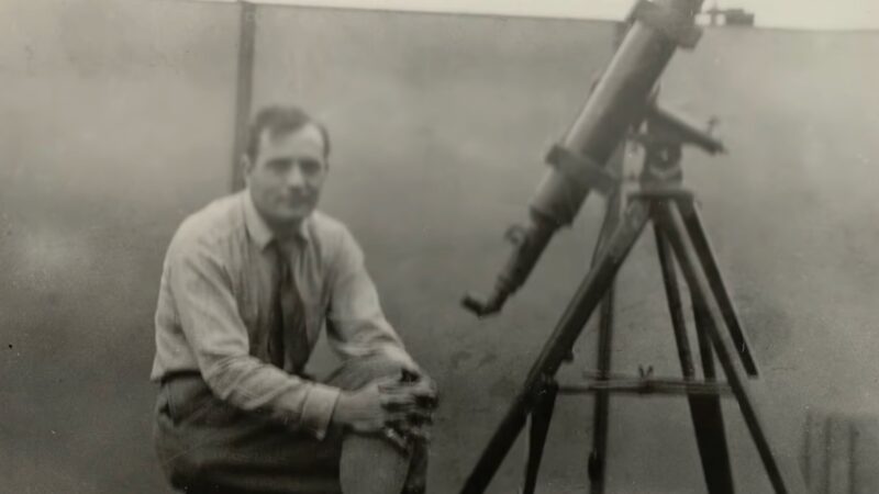 Edwin Hubble: Black-and-white photo of a young man sitting next to a small telescope.