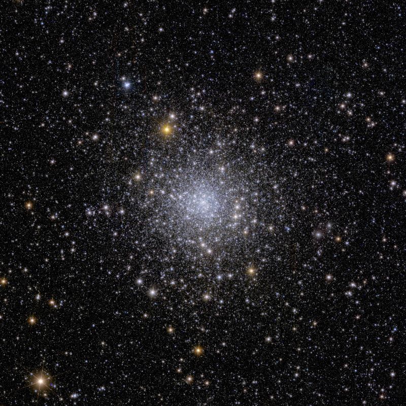 A ball of stars that is compact at the center and more diffuse as you look farther out. The stars are white, bluish and orangish.
