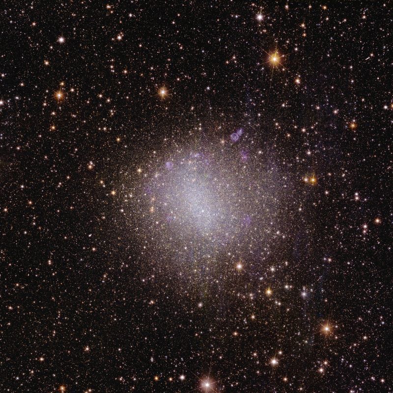A fuzzy galaxy with a brighter vertical bar and diffuse cloud around it sitting in a field of stars.