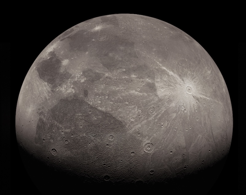 Ganymede: Moon-like dark and light gray sphere with craters and bright white patch with rays extending from it.