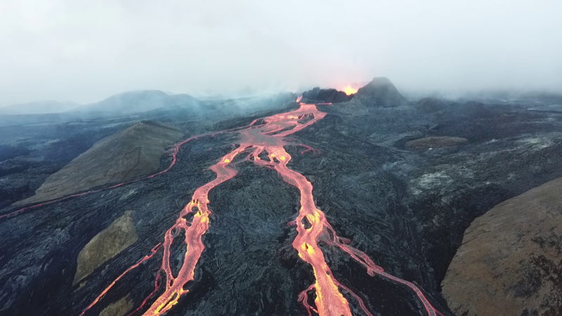 Iceland: Glowing, very liquid appearing orange lava flowing in narrow streams from the top of a volcano.