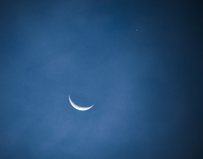 Dark blue sky with a thin crescent moon and a bright dot of light nearby.
