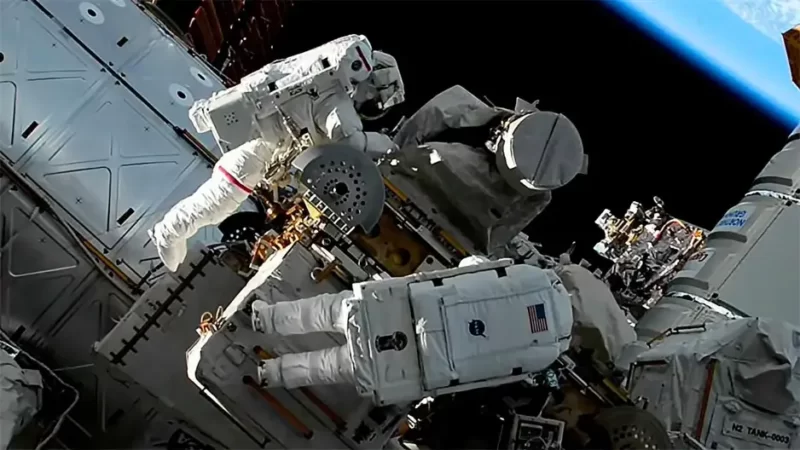 Tool bag: Two astronauts in white spacesuits work on equipment attached to the space station, with edge of Earth barely visible.