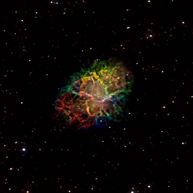 Deep-sky photos: An oblong, multicolor burst of gas and dust in a black starfield.