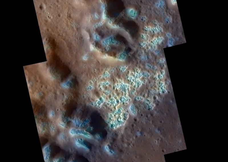 Lumpy brownish terrain with many small irregular pits filled with pale blue, with white edges.
