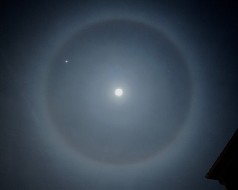 White disk of full moon, near a white dot (Jupiter), all enclosed by a large misty halo.