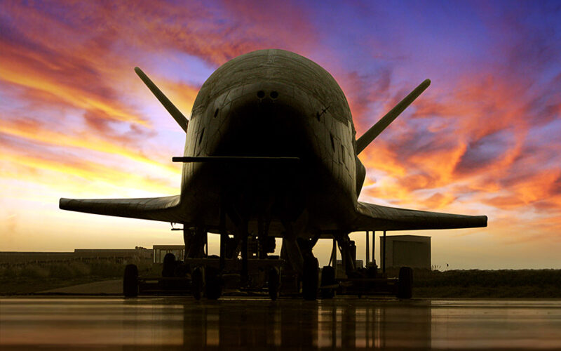 Airplane-like spacecraft in silhouette on wet runway at sunset.
