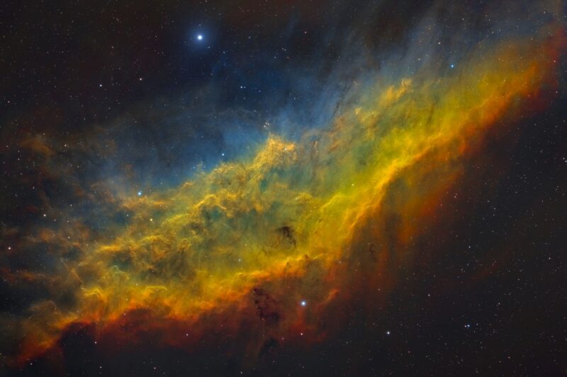 Elongated nebulosity in blue, yellow and red with a sprinkling of faint stars.