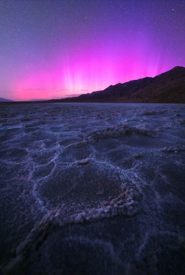 Glowing pink and purple on horizon and curious polygonal salt formations on the desert floorr in the foreground.