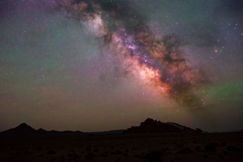 The Milky Way as a dark cloud of gas with bright spots in the night sky over a dark desert scene.