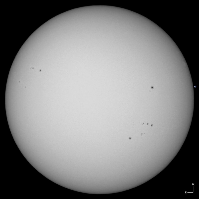 The sun, seen as a large white sphere with small dark spots.