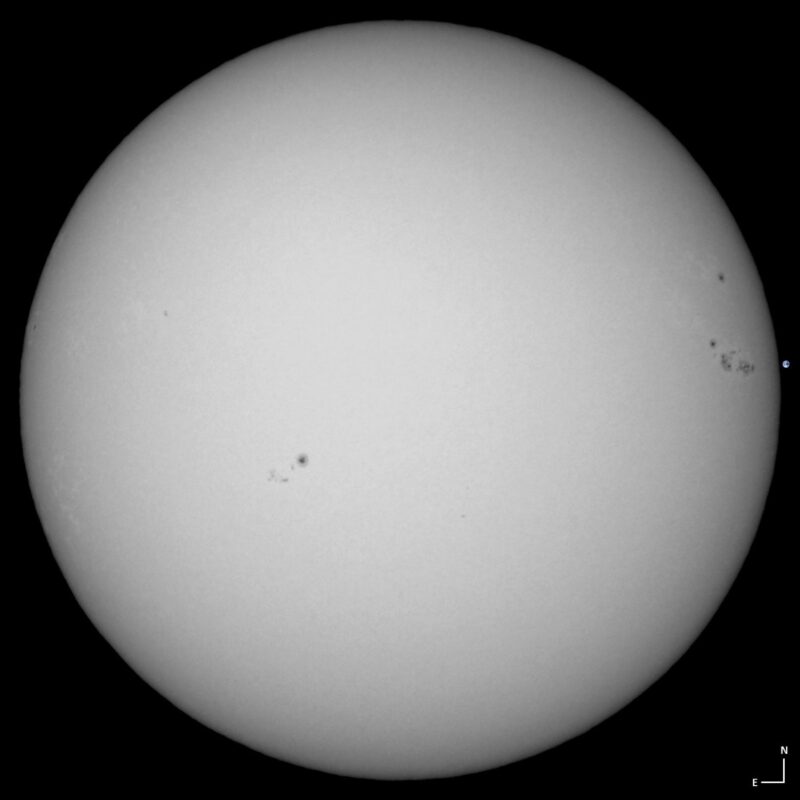 The sun, seen as a large white sphere with small dark spots.