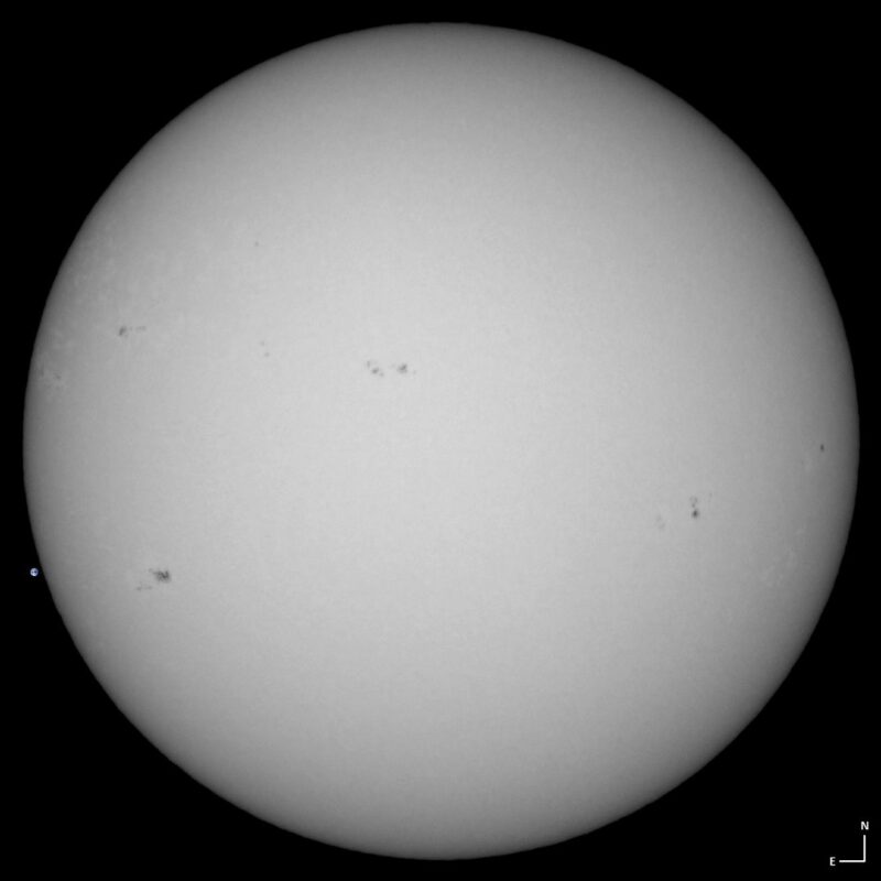 The sun, seen as a large white sphere with small dark spots.
