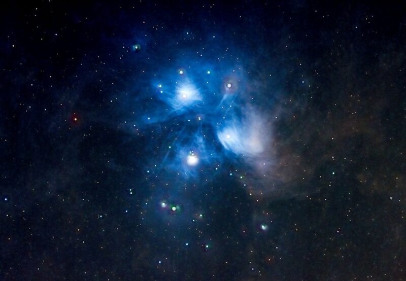 Large area of wispy glowing blue clouds with bright stars immersed within.
