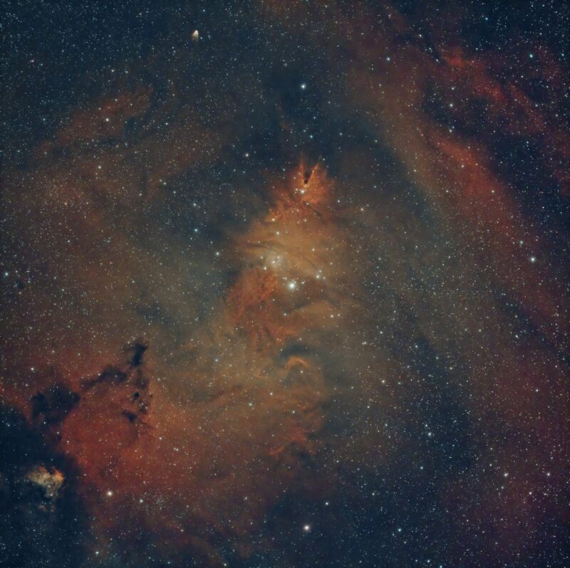 Large, reddish clouds with dark globs and streaks, in star field.