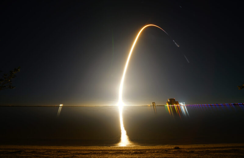 Spaceplane: Illuminated curve of a rocket launch, over water.