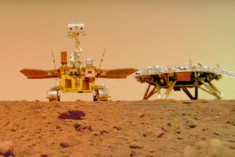 Zhurong rover: Robotic vehicle with wheels and solar panels next to another machine on legs, on reddish rocky ground.