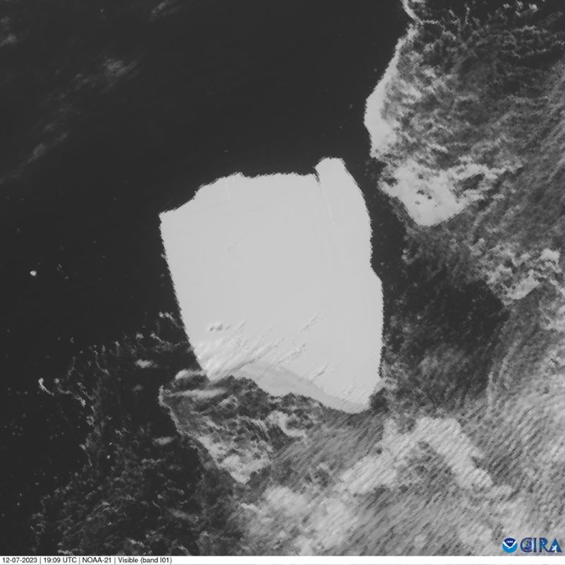 Satellite view of an irregular chunk with low features on its surface surrounded by dark water and some rippling clouds.