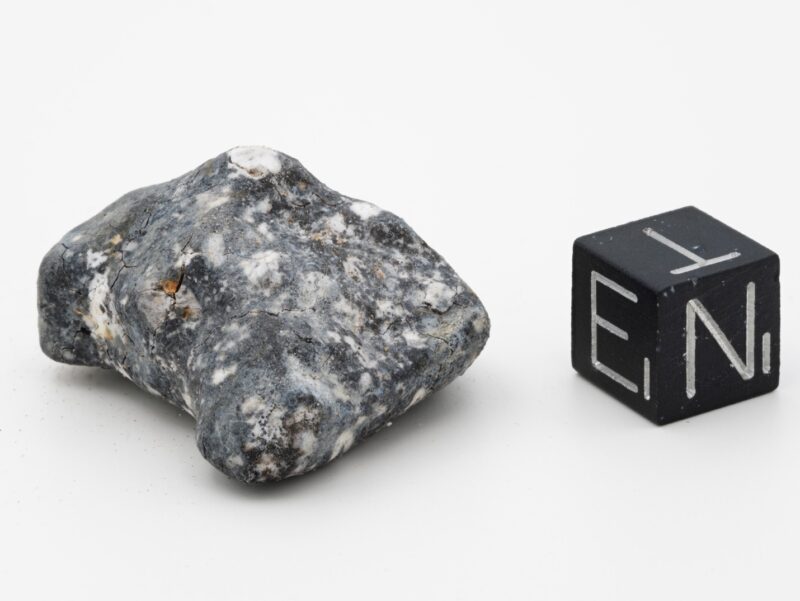 Asteroid: Irregular gray and white mottled rock next to a small black cube with white letters on it.