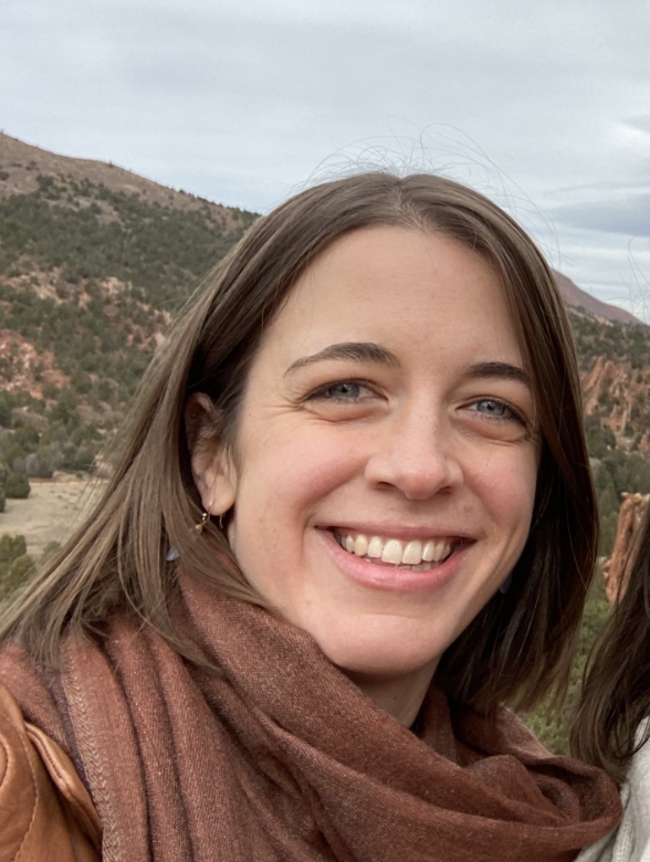 Smiling young woman with long, straight brown hair and a scarf around her neck.