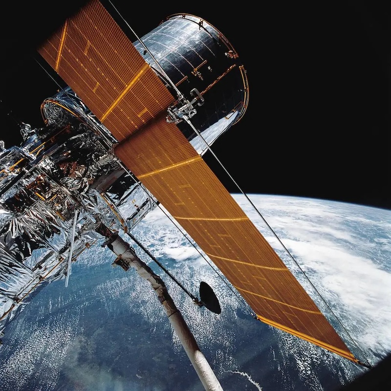 Shiny silver cylindrical spacecraft with large solar panels floating above Earth.