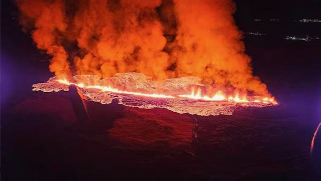 Iceland volcano: In a dark scene, orange smoke boils upward from a line of spouting lava glowing white-hot.