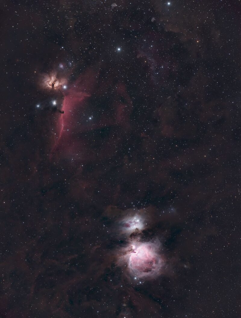 Two clouds of bright nebulosity (the one at top red, the one at bottom white and pink) over a multitude of distant stars.