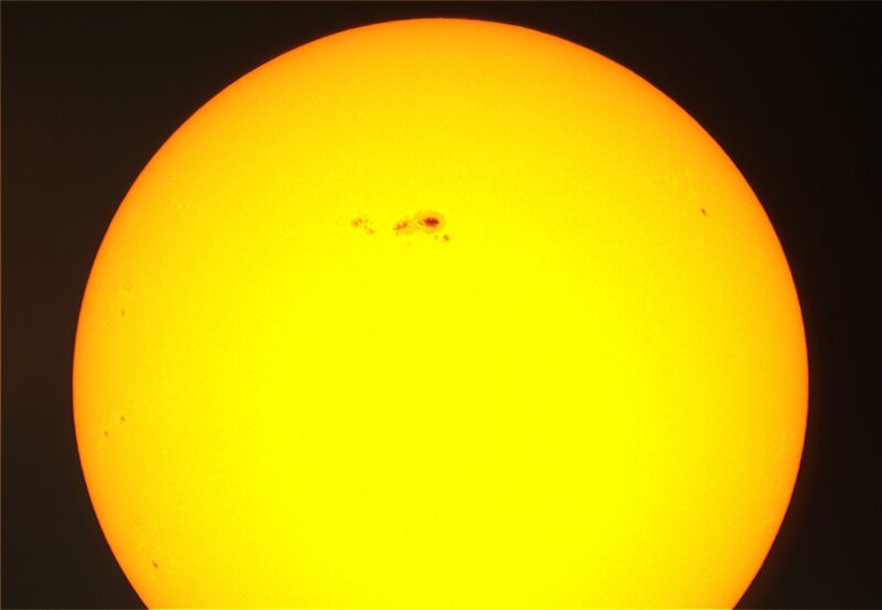 The sun, seen as a sectional yellow sphere with sparse dark spots.