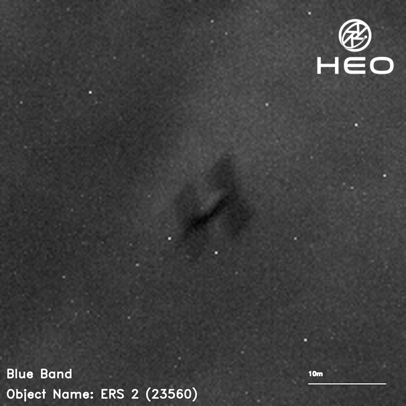 Blurry image of satellite with cylinder connecting wide square part at each end, on staticky background.