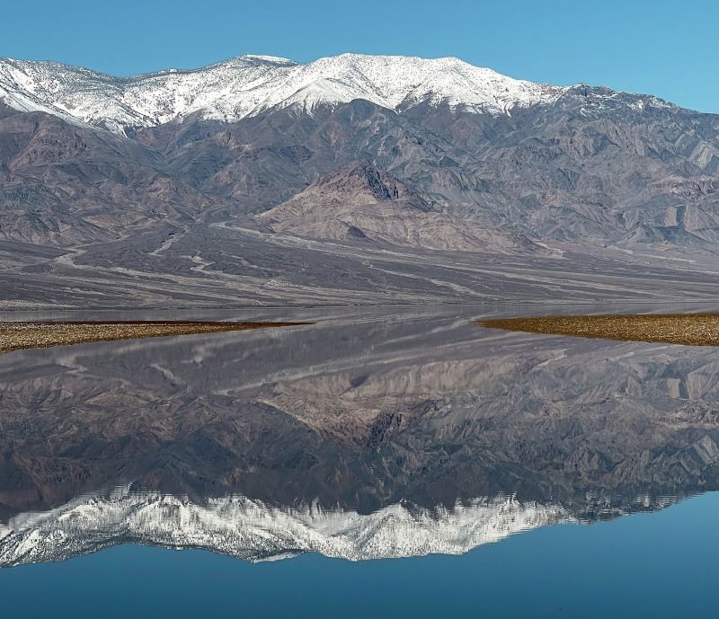 A grayish mountain with a white cap reflected perfectly in water.