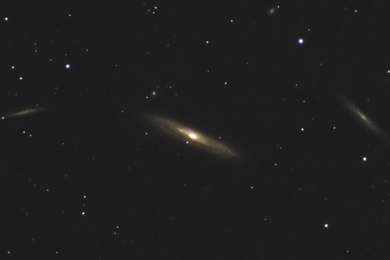 A nearly edge-on spiral galaxy with dim galaxies on either side.