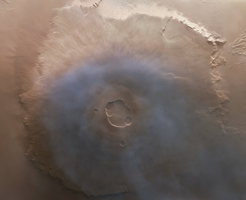 Large volcano on brown terrain seen from above, with wide slopes and distinct central crater.