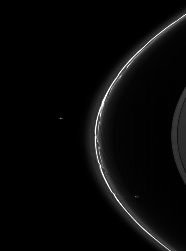 Long bright thin arc with 2 tiny oval objects on either side of it, on black background.