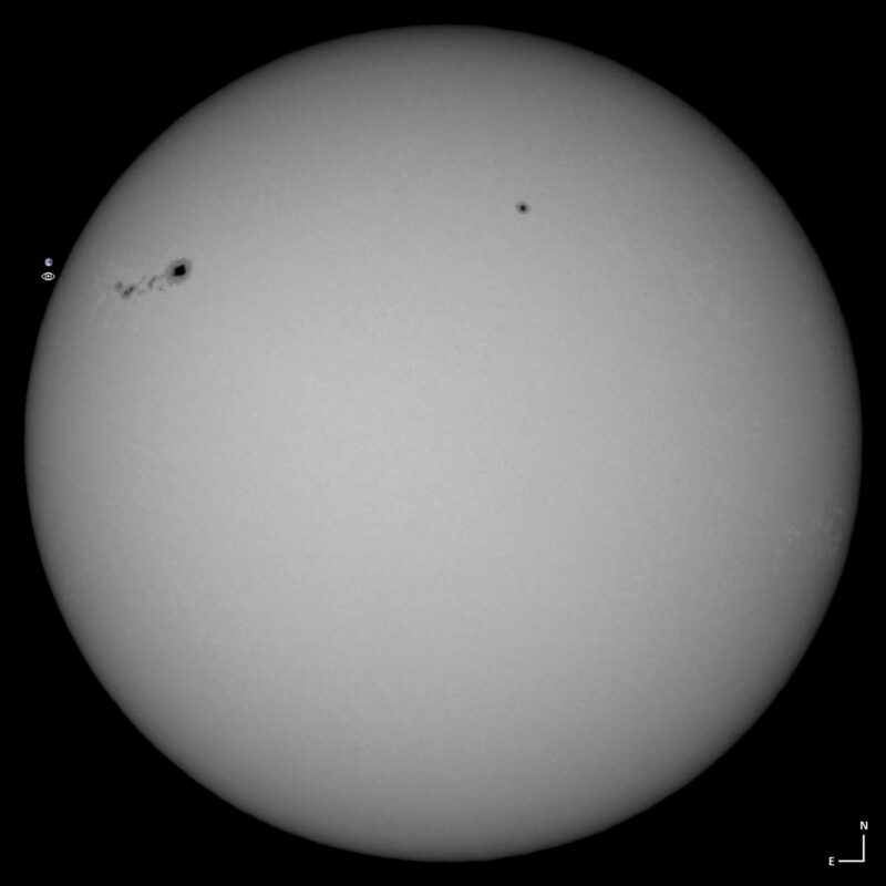 The sun, seen as a large white sphere with small dark spots.