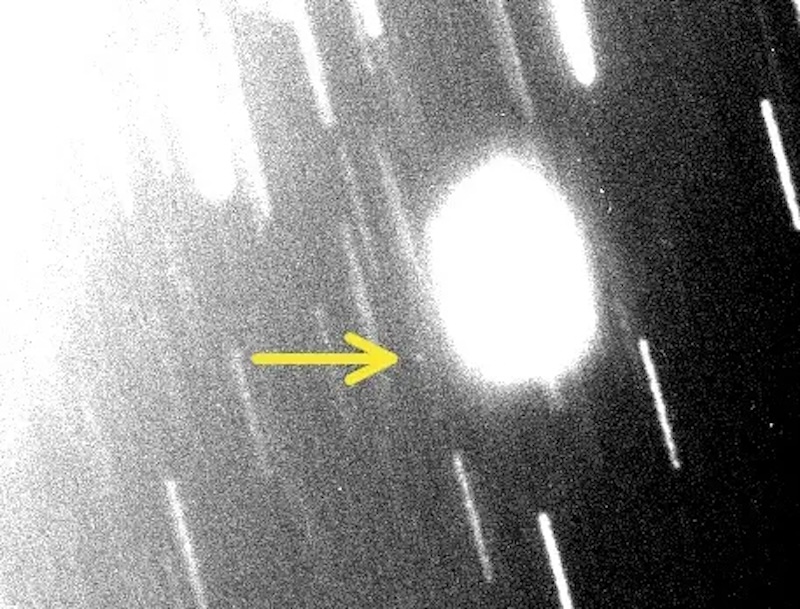 Bright oval shape among many slanted bright and faint lines, with arrow pointing to tiny faint dot.