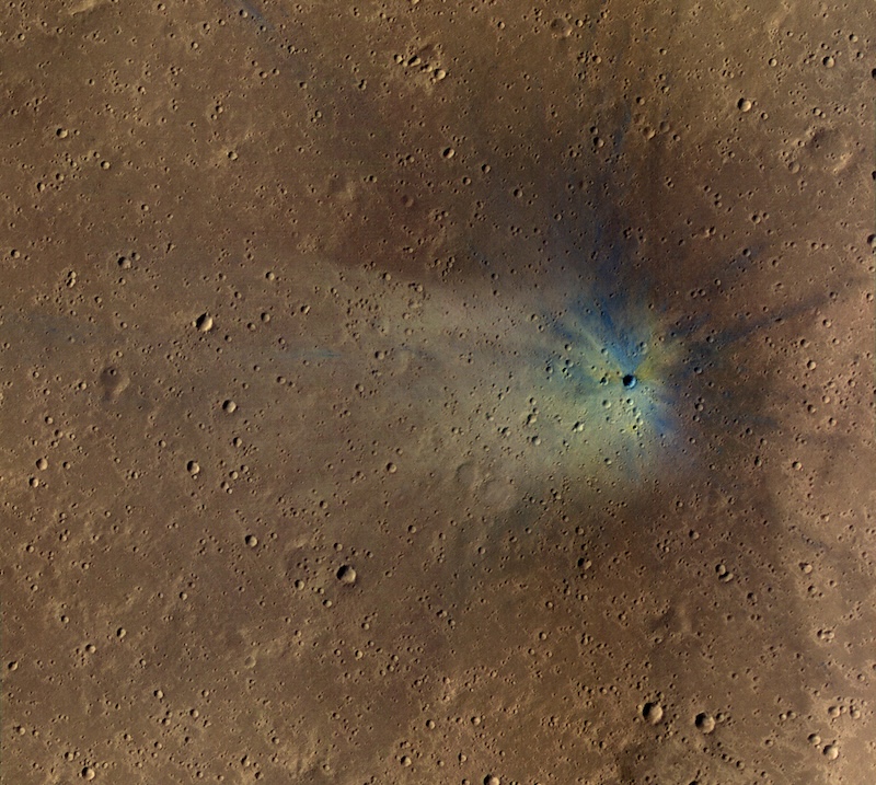 Brownish terrain with many small craters. One crater has colorful streaks around it.