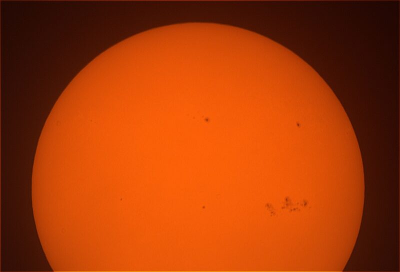 The sun, seen as a sectional orange sphere with small dark spots.