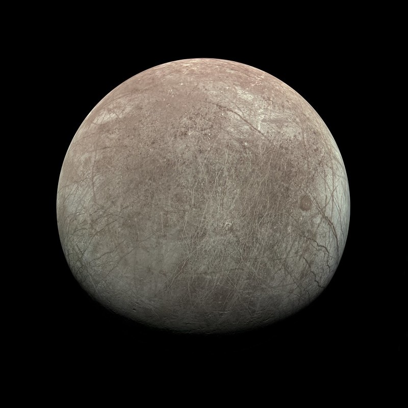 Moon-like body in space with many cracks on its tan-white surface.