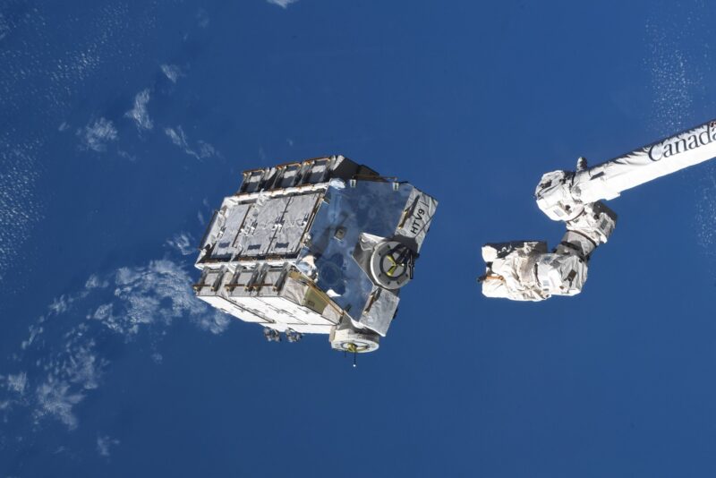 Big white blocky object next to an arm of the space station with the blue background of Earth below.