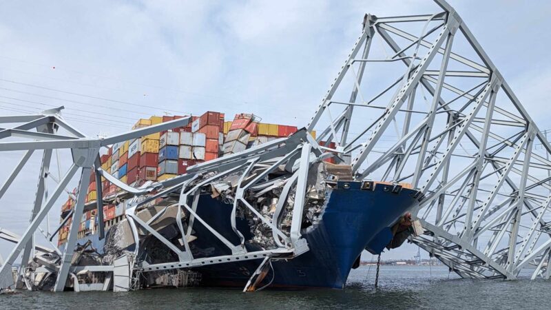 Collapsed bridge pieces lying on top of a ship stacked with containers.